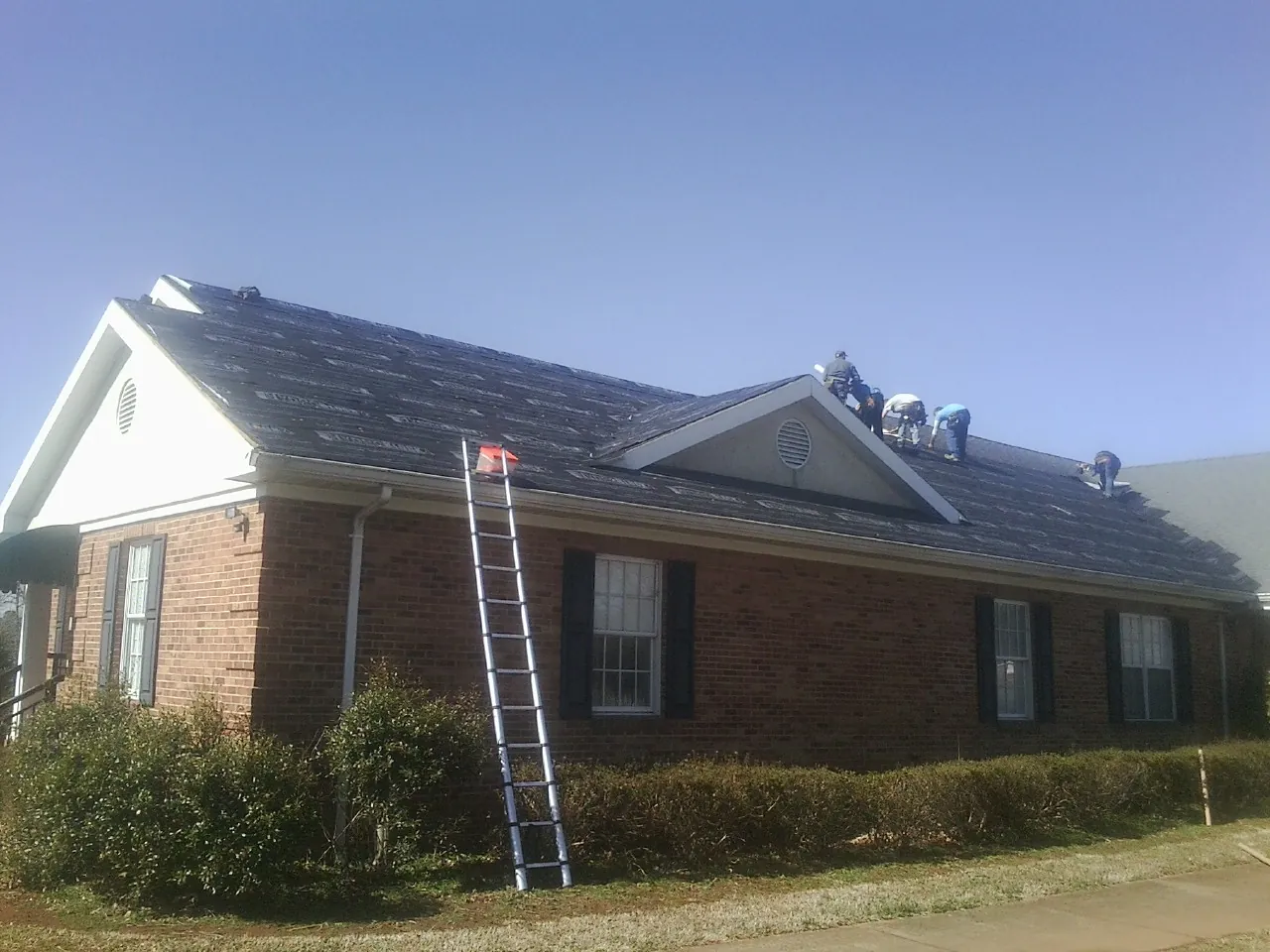 Crew tearing shingles off a brick ranch roof with a ladder set — Metal Roof Repair work by our crew in Mc Lean