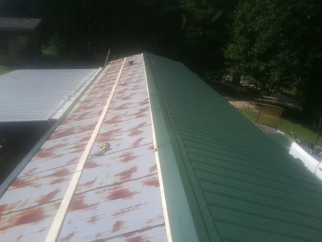 Old rusted panels beside newly installed green metal roofing — Wind Damage Roof Repair by Roofing Brothers in Mc Lean
