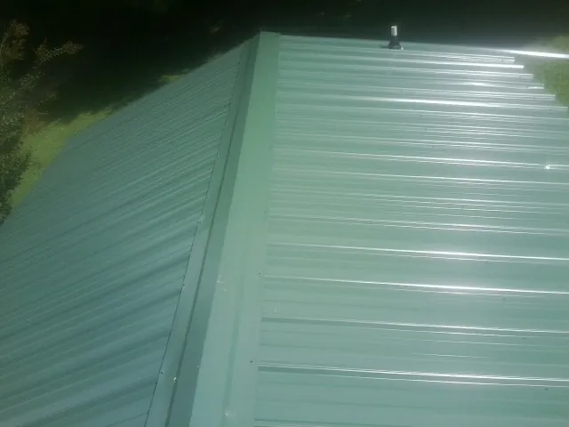 New green metal panels meeting at the ridge of a roof — Flat Roof Repair work by our crew in Mc Lean